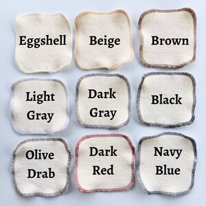 May include: Nine fabric swatches in various colors, including eggshell, beige, brown, light gray, dark gray, black, olive drab, dark red, and navy blue. Each swatch is a square with a contrasting trim around the edges.