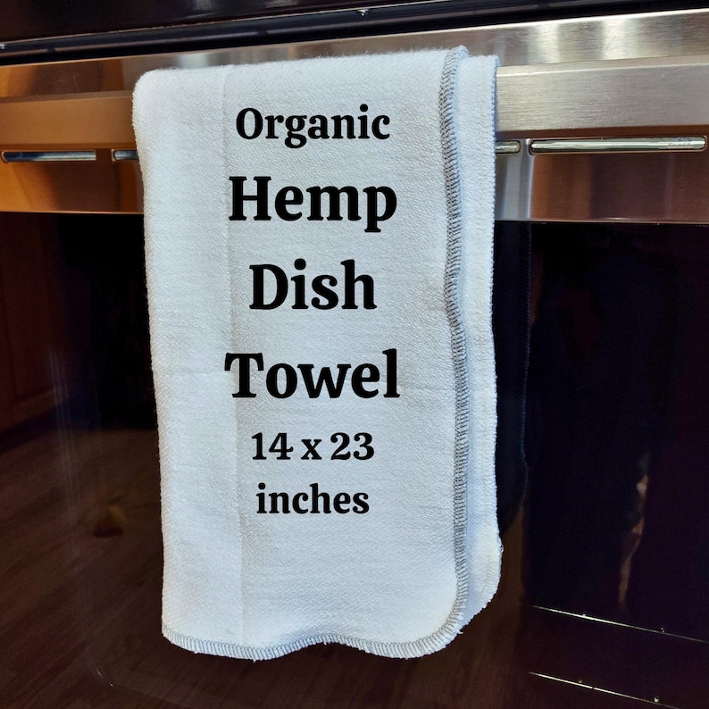 May include: A white organic hemp dish towel with black text that reads "Organic Hemp Dish Towel 14 x 23 inches". The towel is hanging on a silver oven door.