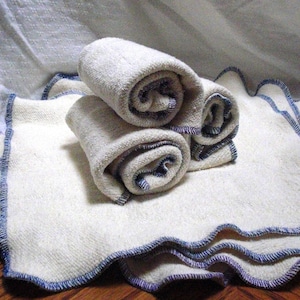 May include: Three white cloth diapers with blue and purple stitching around the edges. The diapers are rolled up and stacked on top of each other.