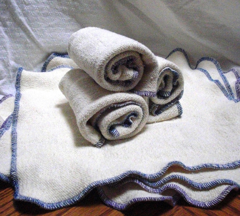 May include: Three white cloth diapers with blue and purple stitching around the edges. The diapers are rolled up and stacked on top of each other.