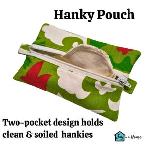 May include: A green and white fabric pouch with a zipper closure. The pouch has a two-pocket design and the text "Hanky Pouch" is printed on the top. The text "Two-pocket design holds clean & soiled hankies" is printed below the pouch. The text "Joy in the Home" is printed in a small box in the lower right corner.