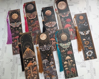 May include: A collection of eight rectangular bookmarks featuring dark illustrations of moths, full moons, mushrooms, and floral elements. Each bookmark is accented with a colourful silk tassel in shades of purple, red, black, gold, or teal.