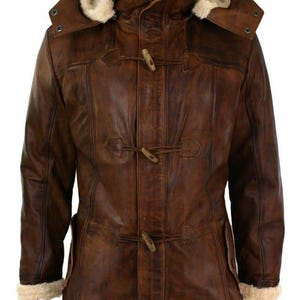 May include: A brown leather duffle coat featuring a hood lined with cream-coloured faux fur. The coat includes three wooden toggle closures down the front, long sleeves with faux fur cuffs, and a high collar that extends into the attached hood.