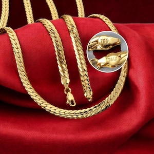 Puede incluir: Un collar de cadena de espiga en tono dorado con cierre de mosquetón. Un detalle circular muestra los componentes del cierre con el texto 750 e ITALY grabado en las superficies metálicas, indicando la pureza y el origen.
