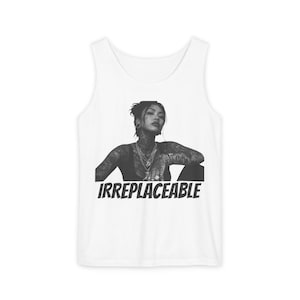 May include: A white tank top featuring a black and white graphic print of a person with extensive tattoos, wearing layered necklaces. The word IRREPLACEABLE is printed in bold black capital letters underneath the graphic on the front of the garment.