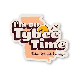 Puede incluir: Una pegatina con el texto "I'm on Tybee Time" en una fuente retro, sobre un contorno color melocotón del estado de Georgia. El diseño incluye un sol, pájaros y las palabras "Tybee Island, Georgia."