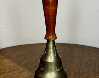 Campana de mano de latón vintage con mango de madera y diseño de pluma grabado.