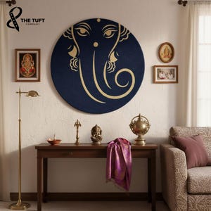 May include: A large circular dark blue wall hanging featuring a gold-colored line art illustration of the deity Ganesha. The artwork is centered above a wooden console table holding a small brass statue, a metallic lamp, and a purple fabric drape.