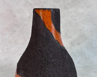 May include: A ceramic vase with a tapered neck and a wide base, featuring a contrasting design of rough, dark charcoal-colored textured surfaces and smooth, glossy orange glazed sections that spiral diagonally around the exterior body.