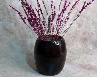 May include: A dark brown, rounded ceramic vase containing a bouquet of dried lavender stems. The lavender features vibrant magenta-colored flower spikes mixed with a few muted, natural-toned stems, creating a contrast against the dark, glossy finish.
