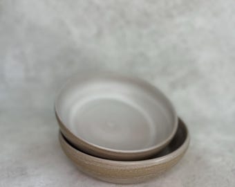 May include: Two stacked ceramic bowls with a smooth, light gray interior and a textured, earthy tan exterior. The bowls feature a rounded shape with a slightly raised rim, showcasing a contrast between the glazed inner surface and the raw outer finish.