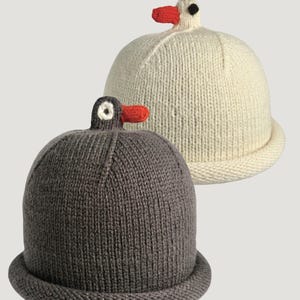 May include: Two knit beanies with rolled brims, one in cream and one in dark gray. Each hat features a small, three-dimensional bird-shaped topper at the crown, complete with a bright orange beak and a circular eye detail.