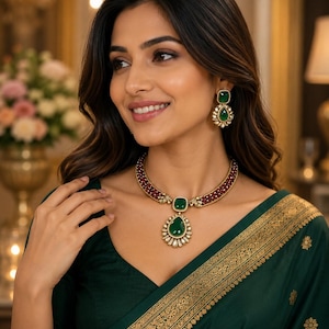 Può includere: Una collana color oro con una pietra verde a goccia circondata da piccole pietre bianche, collegata a una fascia di perline rosso scuro. Gli orecchini abbinati presentano una pietra verde quadrata sopra una pietra verde a goccia.