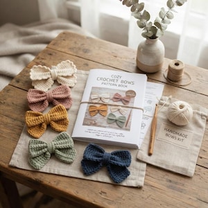 Könnte beinhalten: Ein Häkelset mit einem Anleitungsbuch mit dem Titel Cozy Crochet Bows Pattern Book, fünf gehäkelten Schleifen in Creme, Altrosa, Senfgelb, Salbeigrün und Marineblau, einer Holzhäkelnadel und einem Garnknäuel in einem Stoffbeutel.