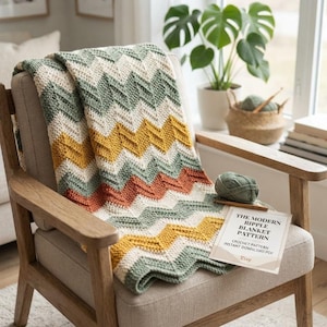 Puede incluir: Una manta de ganchillo con un patrón de ondas en rayas alternas de color verde salvia, crema, amarillo mostaza y naranja terracota. Se incluyen un ovillo de lana verde salvia y un documento titulado The Modern Ripple Blanket Pattern.