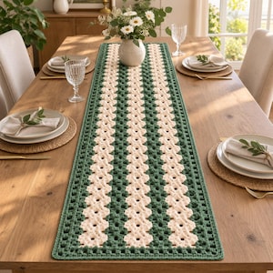 May include: A rectangular crochet table runner featuring alternating vertical stripes of dark forest green and cream white yarn. The design consists of a repeating openwork stitch pattern that runs the entire length of the textile piece.