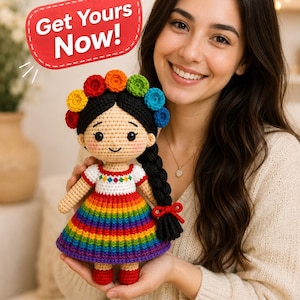 May include: A crochet doll with black hair styled in a braid and a crown of colorful flowers. The doll wears a white top with a multi-colored diamond pattern and a skirt featuring horizontal rainbow stripes. A red speech bubble says Get Yours Now!