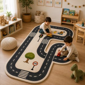 Puede incluir: Una alfombra de color crema con una pista de carretera impresa en gris oscuro con marcas de carril blancas, una ilustración de un árbol verde, un semáforo y una señal de stop roja y blanca. La alfombra tiene una forma curva e irregular.