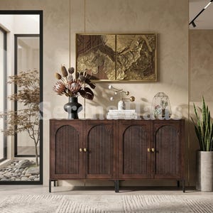 May include: A dark brown wooden sideboard featuring four cabinet doors with vertical fluted panels and small gold knobs. The sideboard stands on black metal legs and is topped with a black vase of dried flowers, a gold sculpture, and books.