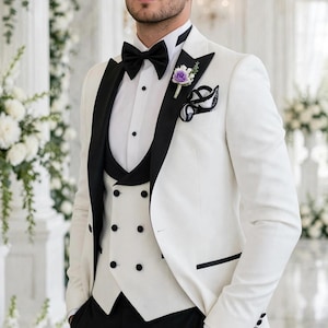 May include: A white tuxedo jacket with black lapels, a white double-breasted vest with black buttons, a white dress shirt, a black bow tie, black trousers, and a purple floral boutonniere. The ensemble includes a black and white pocket square.