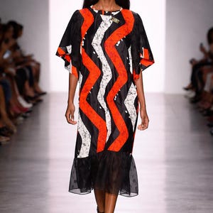 May include: A knee-length dress featuring a bold pattern of vertical orange and white zigzag stripes against a black background. The garment has short, wide sleeves and a sheer black ruffled hemline at the bottom, creating a distinct layered effect.