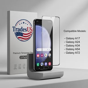 Könnte beinhalten: Ein Smartphone mit einer transparenten Schutzfolie aus gehärtetem Glas davor, auf einem grauen Ständer. Daneben steht eine weiße Produktverpackung mit der Aufschrift TradesUSA Premium Tempered Glass 2-Pack und Kompatibilitätsliste für Galaxy A17, A24, A34, A54 und A72.