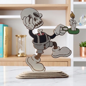 Puede incluir: Una figura plana de madera recortada y superpuesta de un esqueleto de dibujos animados con la cabeza separada, que lleva pantalones cortos y guantes, sosteniendo una vela encendida en un soporte verde. La figura está montada sobre una base ovalada.