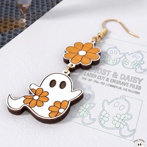 Puede incluir: Un pendiente colgante con forma de fantasma blanco y detalles de flores naranjas, unido a un pendiente de flor naranja. Descansa sobre una hoja impresa con el texto GHOST & DAISY LASER CUT & ENGRAVE FILES SVG DXF PNG PDF.