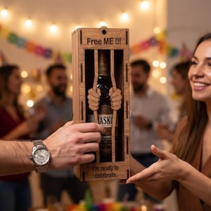 Peut inclure: Une boîte cadeau rectangulaire en bois contenant une bouteille en verre, avec des lattes verticales et des mains en bois sculpté agrippant les barreaux. La boîte porte l'inscription Free ME !!! en haut et I'm ready to celebrate. en bas.