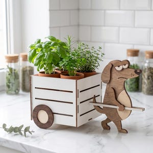 May include: A white wooden crate planter with horizontal slats, featuring a brown wooden dog figure pulling the cart. The planter holds four small terracotta pots containing green herbs. The dog figure has a light brown belly and dark brown ears.