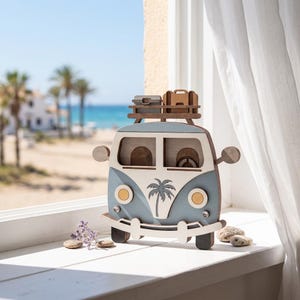 Pode incluir: Uma figura decorativa de madeira em forma de carrinha em azul claro e branco, com um gráfico de palmeira na frente, faróis redondos, espelhos laterais e um suporte de tejadilho com duas pequenas malas, com um design plano e em camadas.