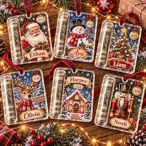 May include: Six rectangular clear acrylic Christmas ornaments featuring a side slot for rolled currency. Each ornament displays a unique holiday scene including Santa, a snowman, a tree, a reindeer, a gingerbread house, or a nutcracker with the year 2026.