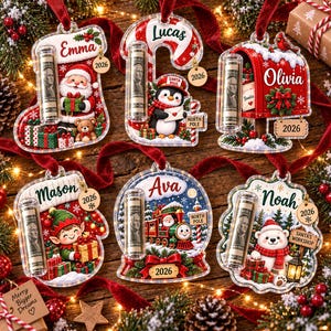 May include: Six clear acrylic Christmas ornaments featuring festive designs including a stocking, candy cane, mailbox, mitten, snow globe, and bear, each personalized with a name, a 2026 charm, and a clear tube containing a rolled dollar bill.
