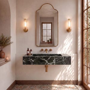 Può includere: Un lavabo rettangolare a parete in marmo verde scuro con venature bianche, dotato di rubinetteria dorata, uno specchio ad arco con cornice dorata abbinata e due applique cilindriche in vetro montate su una parete chiara.