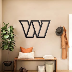 May include: A large, black, geometric wall-mounted letter W sign with a bold, angular design. The letter features sharp, clean lines and a flat, matte finish, serving as a prominent decorative element mounted centrally on a plain wall surface.