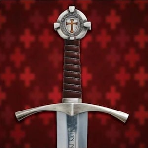 May include: A sword featuring a silver-toned pommel with a central shield emblem displaying a red cross. The grip is wrapped in dark brown leather with a spiral pattern. A wide, curved silver crossguard sits above a steel blade with visible text.