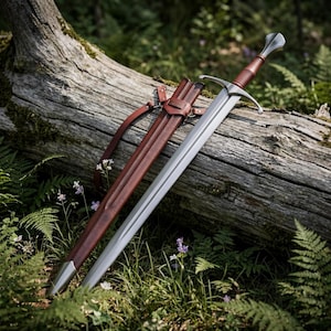 Puede incluir: Una espada larga de acero con hoja plateada pulida, guarda transversal y empuñadura envuelta en cuero marrón oscuro. La espada incluye una vaina de cuero marrón oscuro a juego con contera de metal y una correa de cuero integrada.
