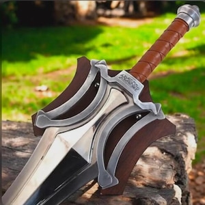May include: A sword with a polished silver-colored metal blade and a crossguard featuring intricate silver metal filigree over a dark wood base. The handle is wrapped in brown leather with a silver-colored pommel at the end of the grip.