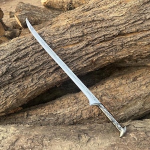 Könnte beinhalten: Ein silberfarbenes Schwert mit einer geschwungenen, einschneidigen Klinge, die entlang der Hohlkehle mit komplizierten Ätzmustern versehen ist. Der Griff ist metallisch mit detaillierten Gravuren und einem ausgestellten Knauf.