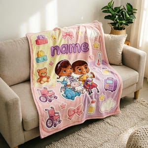 May include: A soft fleece blanket featuring a pastel yellow and pink background with the word name printed in purple. The design includes cartoon characters, a teddy bear, wheelchairs, building blocks, bows, stars, and medical equipment icons.