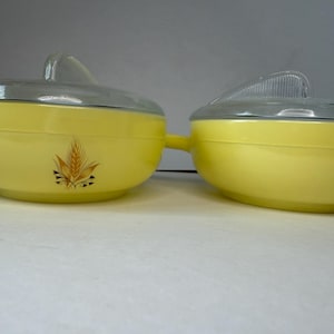Peut inclure: Deux plats de service ronds en verre jaune avec des couvercles en verre transparent. Chaque plat présente une poignée sur un côté et un motif d'épi de blé dans des tons marron et doré sur le devant. Les couvercles ont une poignée nervurée.