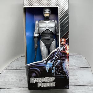 May include: RoboCop action figure in its original box. The figure is silver and black, with a gun in its right hand. The box features the RoboCop logo and an image of RoboCop next to a police car.