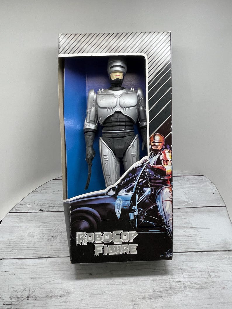 May include: RoboCop action figure in its original box. The figure is silver and black, with a gun in its right hand. The box features the RoboCop logo and an image of RoboCop next to a police car.