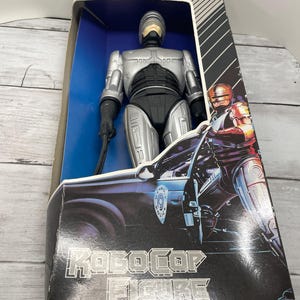 May include: A silver and black Robocop action figure in its original packaging. The box features the words "Robocop Figure" in silver lettering, along with an image of Robocop and a police car. The figure is visible through a clear plastic window.