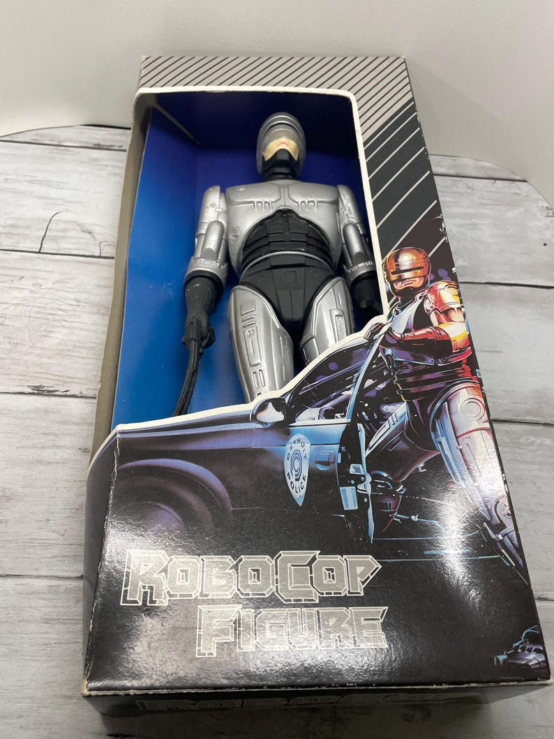 May include: A silver and black Robocop action figure in its original packaging. The box features the words "Robocop Figure" in silver lettering, along with an image of Robocop and a police car. The figure is visible through a clear plastic window.