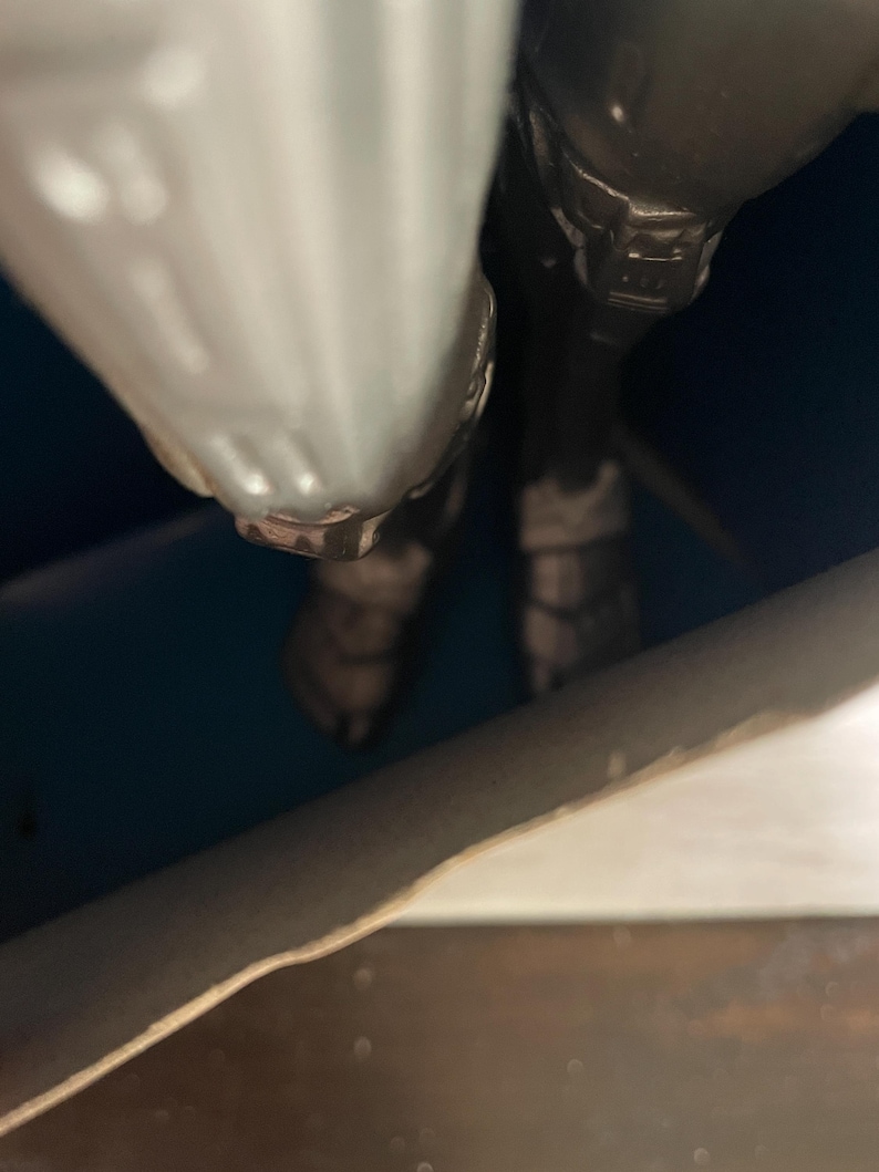May include: Close-up of a metallic gray action figure. The figure's legs and lower torso are visible, with detailed armor and boots. The figure is positioned against a dark blue background.