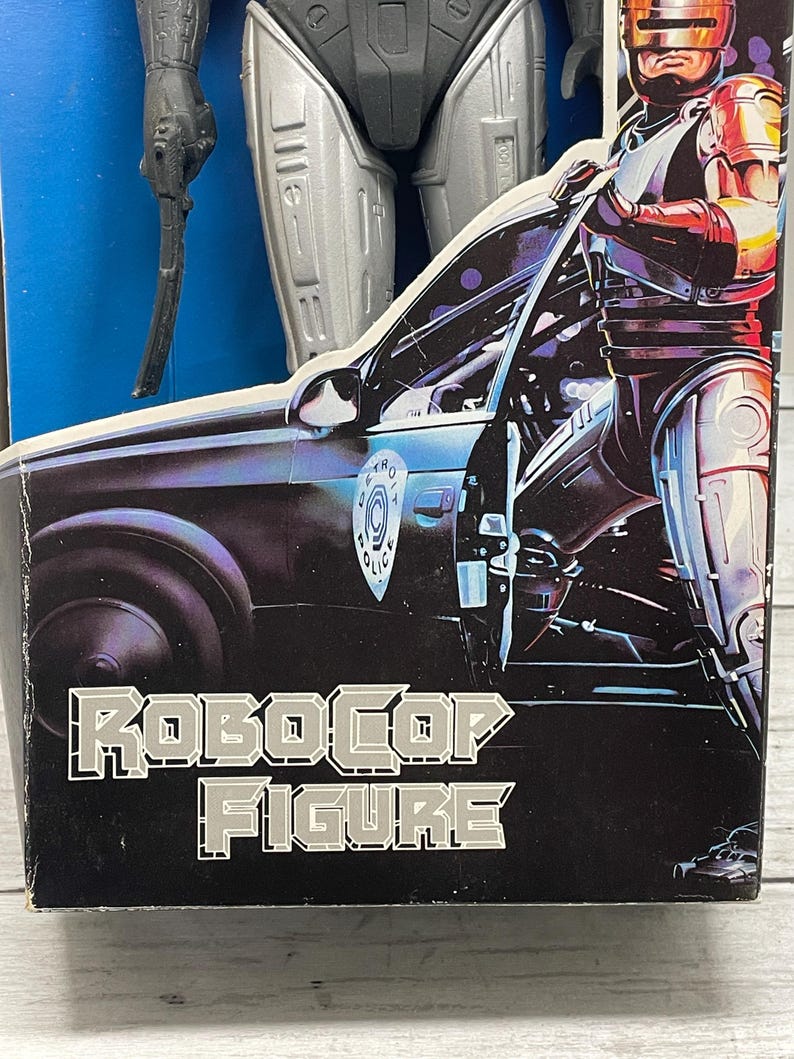 May include: A RoboCop action figure in its original packaging. The box features a graphic of RoboCop standing next to a police car. The words "RoboCop Figure" are printed in silver block letters on a black background.