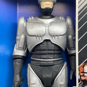 May include: A silver and black Robocop action figure in its original packaging. The figure has a helmet, chest armor, and black accents. The packaging is blue with black and white stripes.