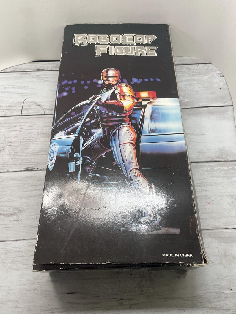 May include: A Robocop action figure box. The black box features the words "ROBOCOP FIGURE" in silver lettering. The image on the box shows Robocop standing next to a police car. The box is marked "MADE IN CHINA".