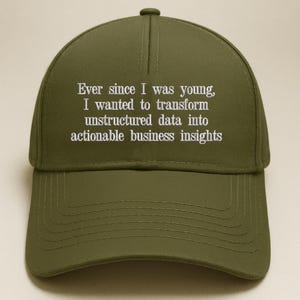 Op de afbeelding: Een olijfgroene baseballpet met witte geborduurde tekst die luidt: Ever since I was young, I wanted to transform unstructured data into actionable business insights. De pet heeft een gestructureerde kroon en een gebogen klep.